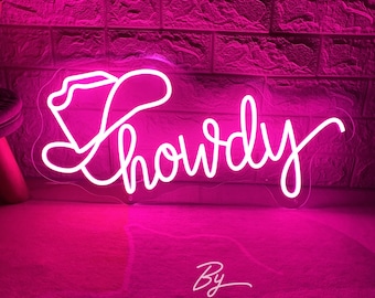 May include: A neon sign in bright pink, featuring the word "Howdy" in a cursive font, with a cowboy hat incorporated into the design. The sign is illuminated against a brick wall background. The text "By ZP Neon Custom" is at the bottom.