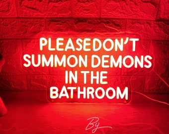 May include: A red neon sign with the text "PLEASE DON'T SUMMON DEMONS IN THE BATHROOM." The sign is illuminated against a red brick wall. The words "By ZP Neon Custom" are written in cursive at the bottom.
