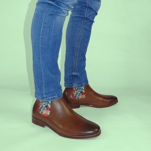 May include: Brown leather ankle boots with a floral patterned fabric lining the top of the boot. The boots are worn with blue jeans.