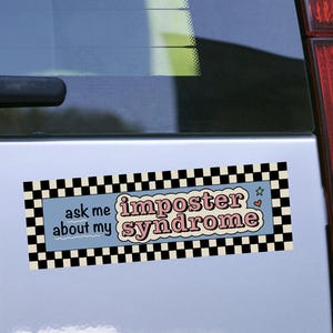 Könnte beinhalten: Rechteckiger Aufkleber mit dem Text "ask me about my imposter syndrome" in einer Retro-Schriftart. Der Aufkleber hat einen hellblauen Hintergrund mit einem schwarz-weißen Schachbrettmuster und einem Sternmuster.