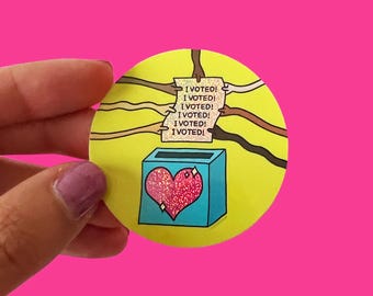 May include: A yellow circle sticker with a blue and pink heart-shaped ballot box.  Multiple hands of different skin tones are reaching into the box with a note that reads "I VOTED!" repeated five times.