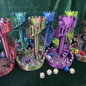 May include: A selection of multi-coloured 3D-printed dice towers. Each tower has a spiral staircase design and a circular base. The towers are in shades of red, blue, green, and purple, with dice scattered around.