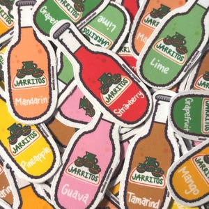 May include: A collection of die-cut stickers shaped like glass soda bottles in various colors. Each sticker features the Jarritos logo and a specific flavor name printed in white text, including Mandarin, Strawberry, Guava, Tamarind, and Lime.