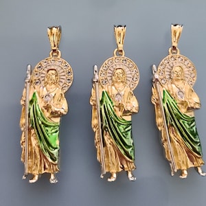 May include: Three gold pendants featuring a religious figure with a green robe and a halo of white stones. The pendants are on a light blue background.
