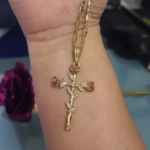 May include: A gold chain necklace with a rose cross pendant. The cross is made of gold and has three roses on it. The roses are a mix of gold and white.