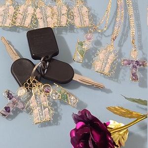 May include: An assortment of handmade jewelry, including cross pendants and necklaces, featuring amethyst and other gemstones. The jewelry is crafted with gold-colored wire and chains. A pair of car keys and a purple rose are also present.