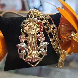 May include: Gold pendant necklace featuring a detailed depiction of the Virgin Mary with red, green, and white gemstones. The pendant is surrounded by gold leaves and a dove.