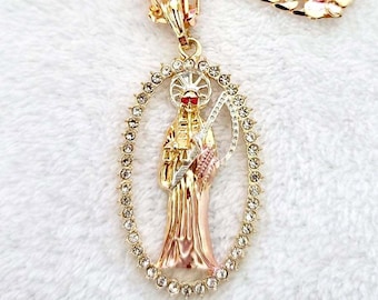 May include: A gold chain necklace with a pendant featuring a detailed depiction of a skeletal figure with a scythe, surrounded by clear rhinestones.