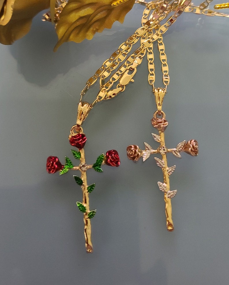 May include: Two gold chains with rose cross pendants. One cross has red roses and the other has pink roses.