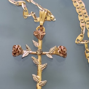 May include: A gold chain necklace with a rose cross pendant. The cross is made of two-toned gold and features three roses.