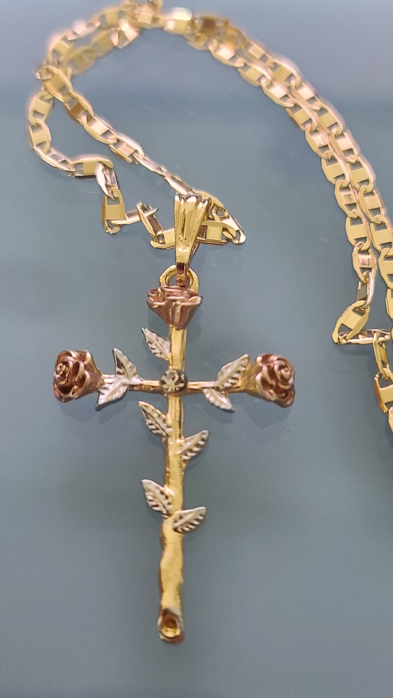 May include: A gold chain necklace with a rose cross pendant. The cross is made of two-toned gold and features three roses.