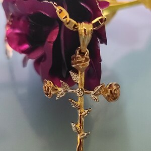 May include: A gold-tone pendant necklace featuring a cross with roses and leaves. The pendant is hanging from a chain.