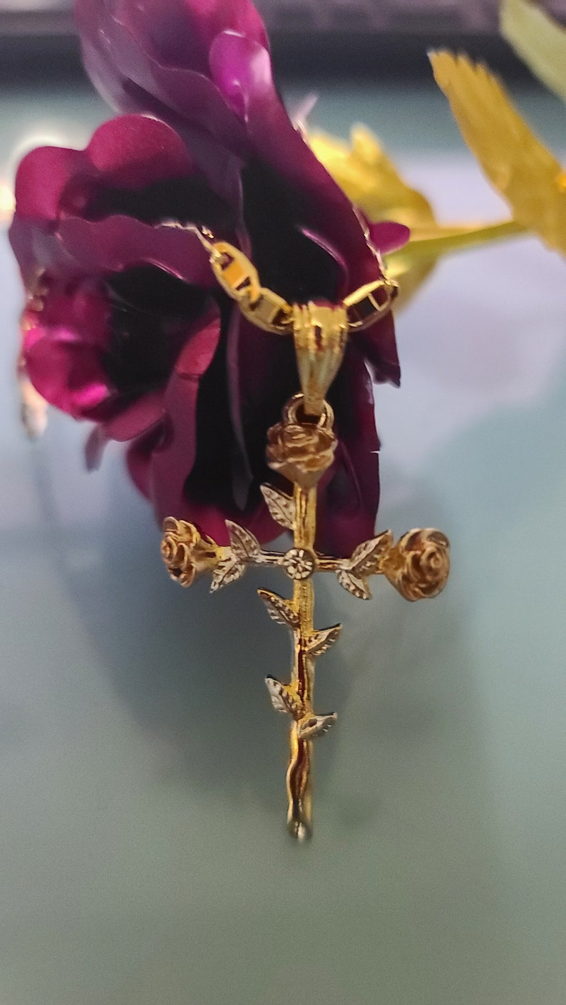 May include: A gold-tone pendant necklace featuring a cross with roses and leaves. The pendant is hanging from a chain.