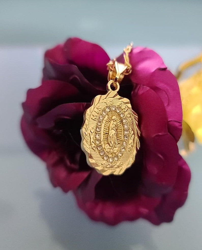 May include: A gold-tone pendant necklace with a detailed oval charm featuring a religious figure surrounded by sparkling rhinestones.