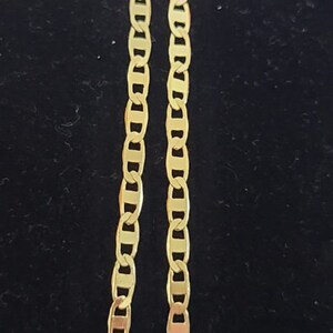 May include: Two gold chains with a mariner link pattern. The chains are lying flat on a black surface.
