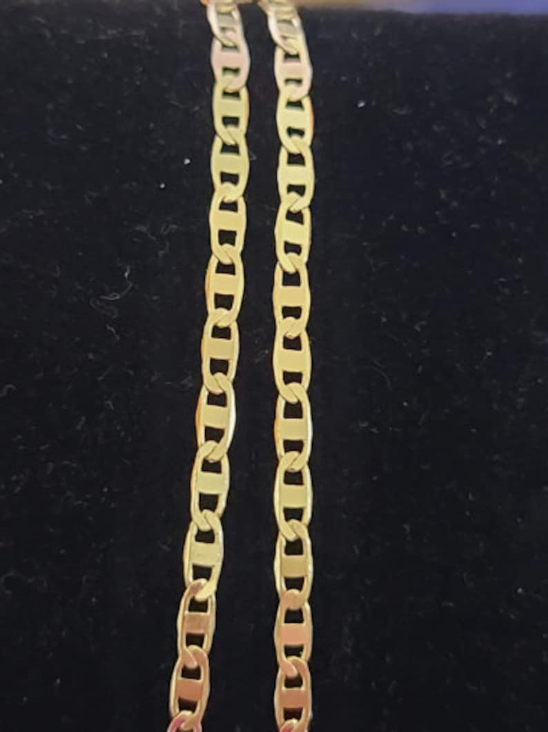 May include: Two gold chains with a mariner link pattern. The chains are lying flat on a black surface.