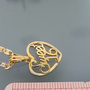 May include: Gold heart-shaped pendant necklace with the word "Sweet" inscribed inside. The necklace is on a gold chain and is next to a ruler.