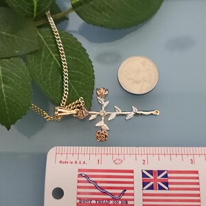 May include: A gold rose cross pendant necklace with a white diamond in the center. The pendant is about 1 inch in length and is shown next to a ruler and a US quarter.