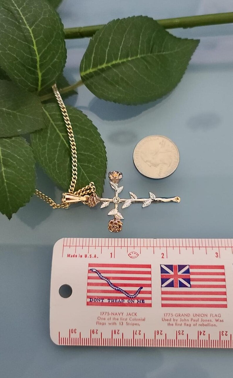 May include: A gold rose cross pendant necklace with a white diamond in the center. The pendant is about 1 inch in length and is shown next to a ruler and a US quarter.