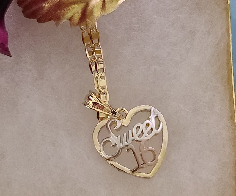 May include: Gold necklace with a heart-shaped pendant that says "Sweet 16" in a cursive font.