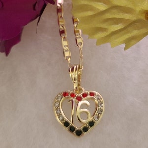 May include: Gold heart-shaped pendant necklace with a number 16 in the center. The heart is decorated with black, red, and clear rhinestones.