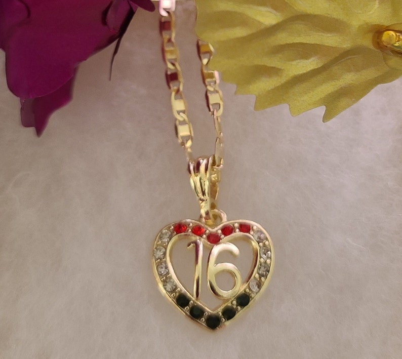 May include: Gold heart-shaped pendant necklace with a number 16 in the center. The heart is decorated with black, red, and clear rhinestones.