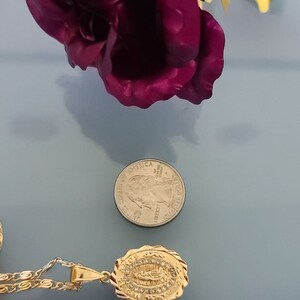 May include: Gold chain necklace with a pendant featuring a depiction of the Virgin Mary surrounded by clear rhinestones. The pendant is about 1 inch in length. The necklace is next to a ruler for size reference.