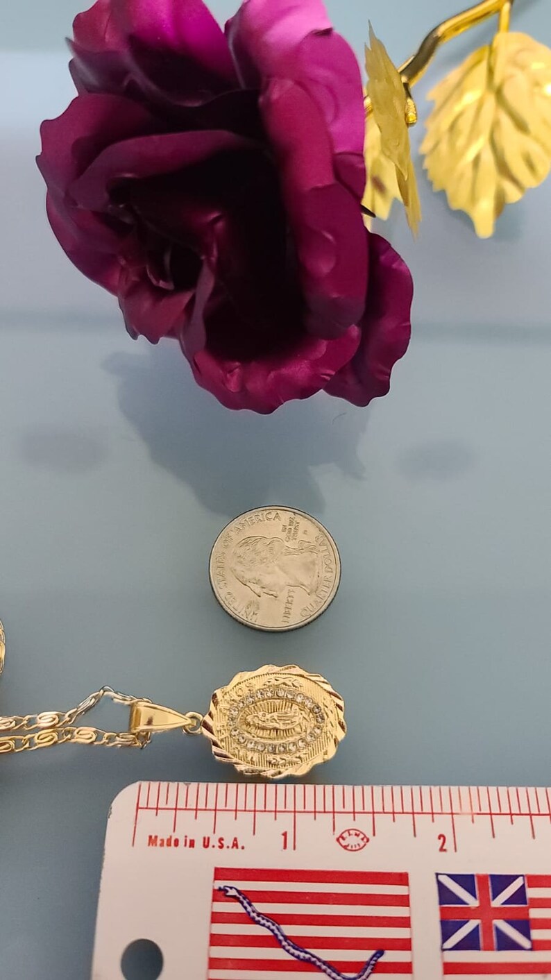 May include: Gold chain necklace with a pendant featuring a depiction of the Virgin Mary surrounded by clear rhinestones. The pendant is about 1 inch in length. The necklace is next to a ruler for size reference.