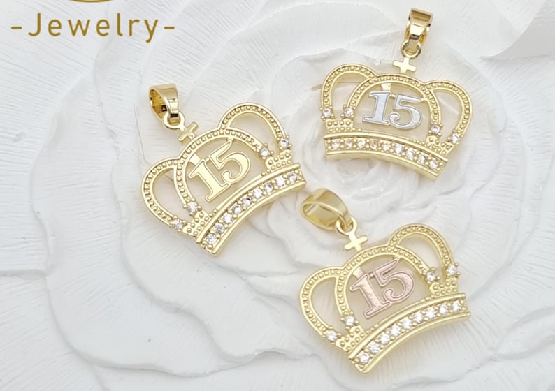 May include: Three gold-toned crown pendants, each featuring the number 15 in the center. The base of each crown is embellished with a row of small, clear, sparkling stones. Each pendant includes a small bail at the top for attachment to a chain.