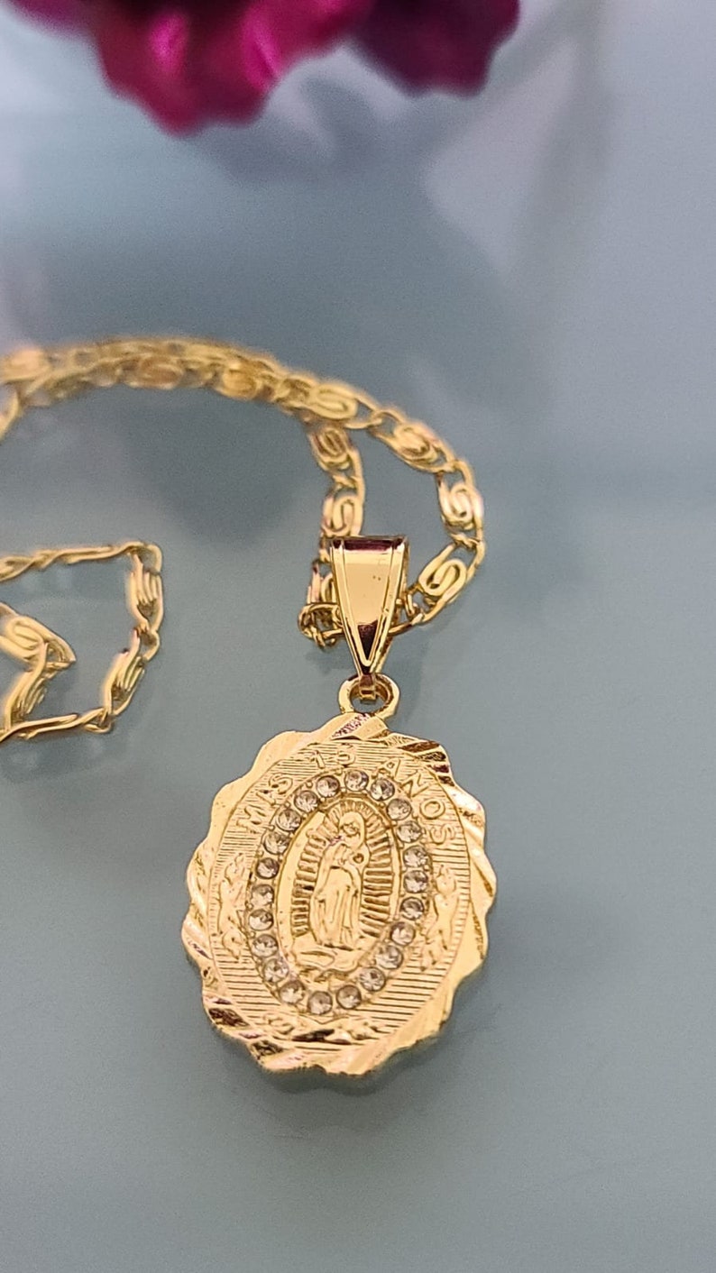 May include: Gold chain necklace with a pendant featuring a depiction of the Virgin Mary surrounded by clear rhinestones. The pendant has the words "MI MADRE" and "AMOR" inscribed on it.