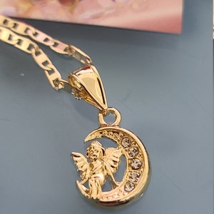 May include: Gold necklace with a pendant featuring a cherub sitting on a crescent moon with clear crystals.