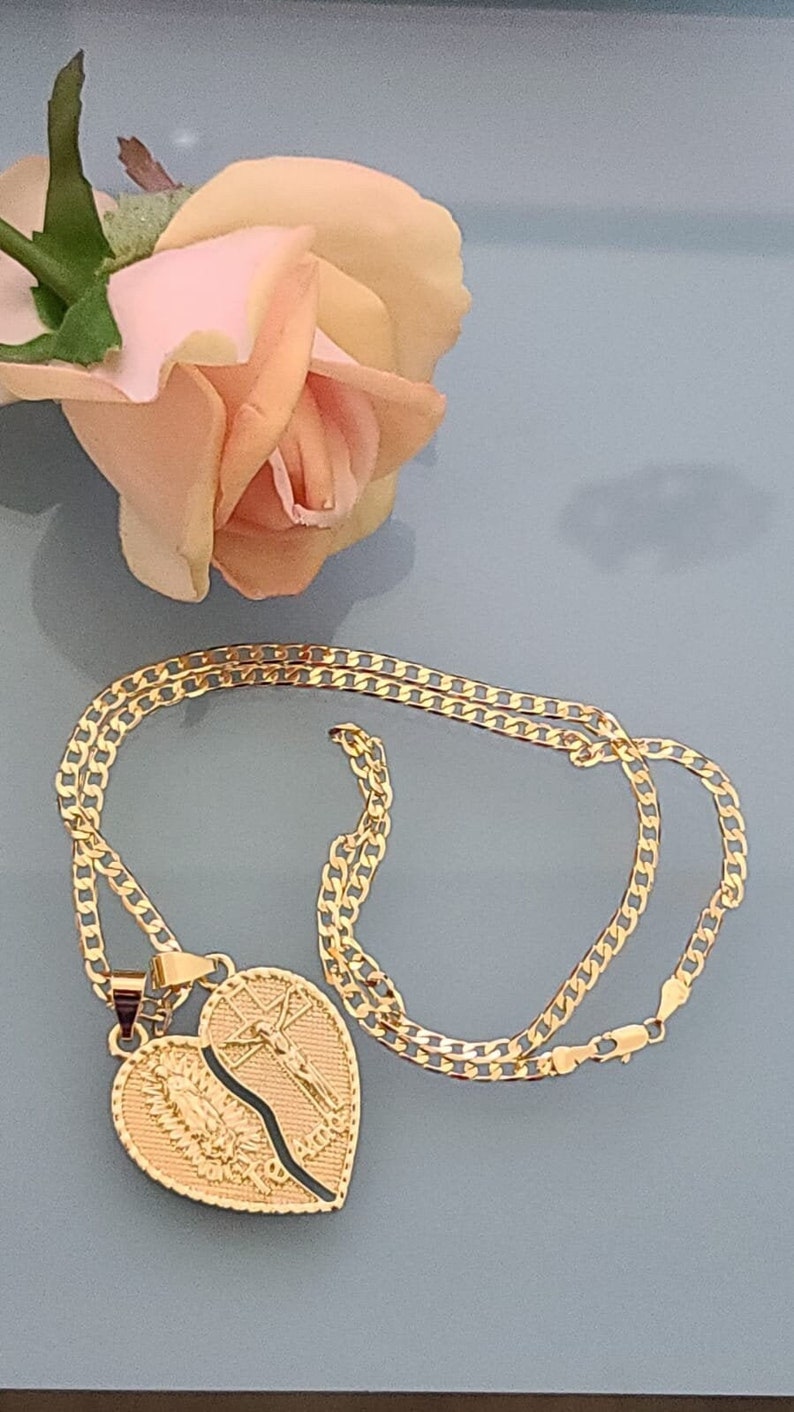May include: A gold chain necklace with a broken heart pendant. The pendant features a depiction of the Virgin Mary on one side and Jesus on the cross on the other side.