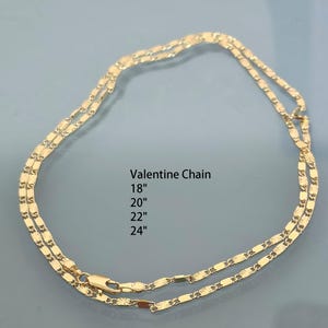 May include: A gold-colored Valentine chain necklace featuring a series of flat, textured links. The text printed in the center reads: Valentine Chain 18", 20", 22", 24". The chain includes a lobster claw clasp closure at the bottom.