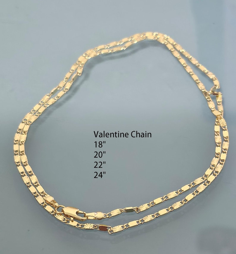 May include: A gold-colored Valentine chain necklace featuring a series of flat, textured links. The text printed in the center reads: Valentine Chain 18", 20", 22", 24". The chain includes a lobster claw clasp closure at the bottom.