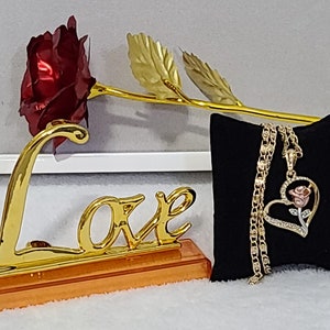 May include: A gold-plated rose with a red velvet rose bud, a gold 'Love' sign, and a gold chain necklace with a heart-shaped pendant featuring a rose design.