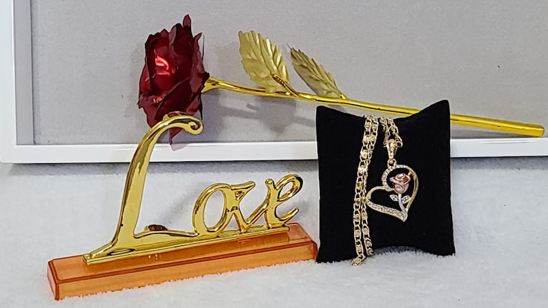 May include: A gold-plated rose with a red velvet rose bud, a gold 'Love' sign, and a gold chain necklace with a heart-shaped pendant featuring a rose design.