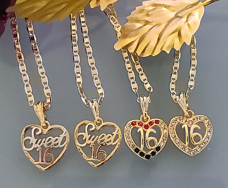 May include: Four gold necklaces with heart-shaped pendants. The pendants feature the words "Sweet 16" in different styles, including one with red and black rhinestones and another with clear rhinestones.