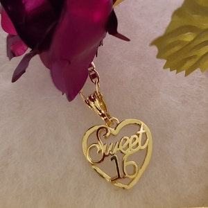May include: Gold heart-shaped pendant necklace with the words "Sweet 16" inscribed inside. The necklace is hanging from a rose.