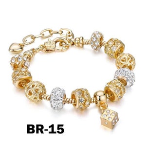 May include: Gold-toned bracelet with various decorative beads, including clear and gold-colored crystals. The bracelet features a charm in the shape of a die. The text "BR-15" is visible.