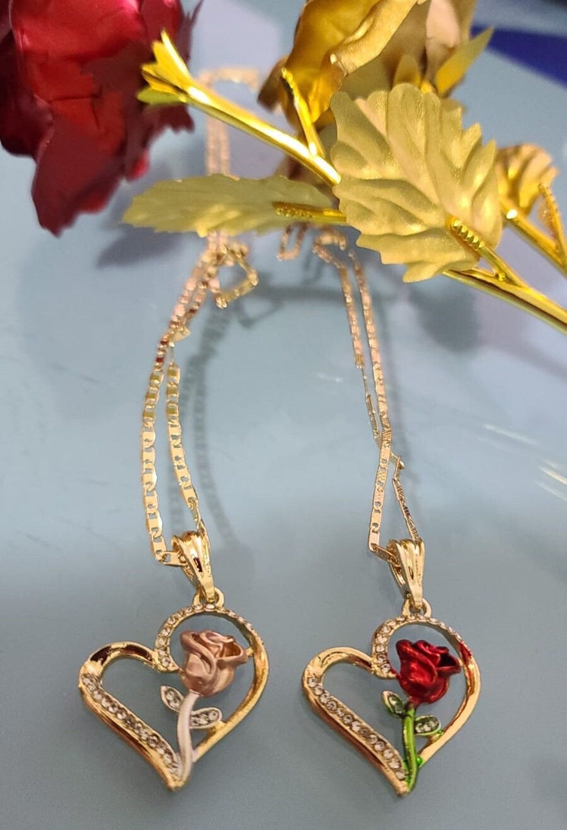 May include: Two gold necklaces with heart-shaped pendants featuring a rose design. One rose is pink and the other is red.