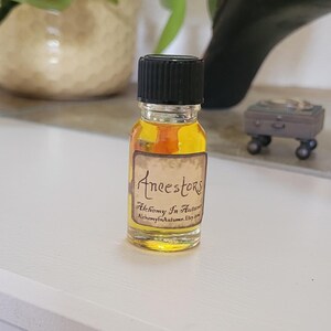 May include: A small amber glass bottle with a black cap and a label that reads "Ancestors Alchemy In Autumn AlchemyInAutumn.Etsy.com".