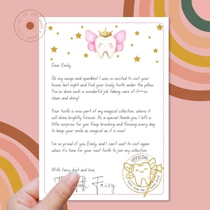 Puede incluir: Una carta de la hada de los dientes rosa y dorada con un mensaje escrito a mano para Emily. La carta dice: "&iexcl;Oh, mis alas y mis brillos! Estaba tan emocionada de visitar tu casa anoche y encontrar tu precioso diente debajo de la almohada. Has hecho un trabajo maravilloso cuid&aacute;ndolo, &iexcl;tan limpio y brillante!" La carta tambi&eacute;n incluye un sello de estrella dorada con el texto "Visita oficial del hada de los dientes".