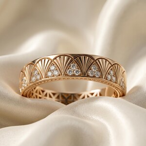 May include: A rose gold bracelet featuring a repeating fan pattern, each fan set with small diamonds. The bracelet is presented on a soft, cream-coloured fabric, emphasising its intricate details and elegant style.