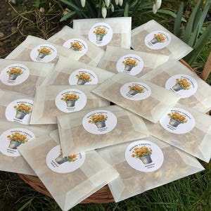 Puede incluir: Una cesta llena de pequeñas bolsas de papel blanco, cada una con pétalos de flores secas. Las bolsas están etiquetadas con una pegatina redonda que dice "Confetti de boda Pétalos de caléndula".