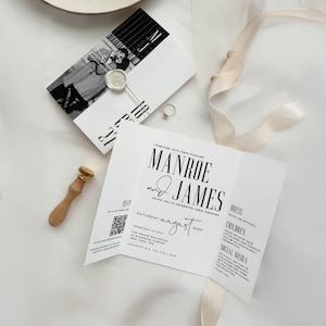 Może przedstawiać: Zestaw zaproszeń ślubnych z białym zaproszeniem i czarnym tekstem, zawierający imiona "Manroe i James" oraz datę "sobota, sierpień 2029". Zestaw zawiera kartę ze zdjęciem, złoty pierścionek, pieczęć woskową i drewnianą pieczątkę.