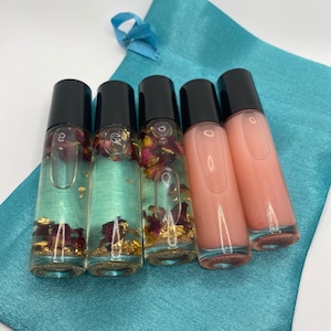 May include: Four small glass bottles with black caps, containing a clear liquid with rose petals and gold flakes. The bottles are arranged in a row on a teal satin bag.