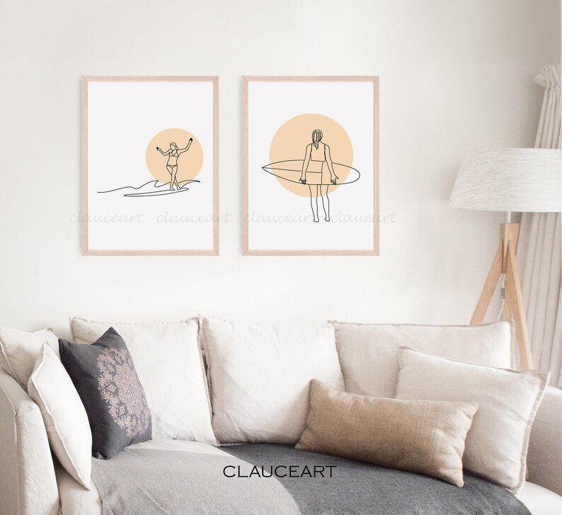 Pu&ograve; includere: Due stampe minimaliste di arte di linea di una ragazza che fa surf con una tavola da surf. Le stampe sono incorniciate in una cornice di legno chiaro e hanno uno sfondo pesca. Le stampe sono appese a un muro bianco sopra un divano beige.