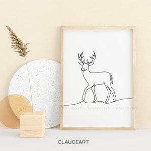 May include: A black and white line drawing of a deer with antlers, framed in a light wood frame. The frame is sitting on a white surface with a beige background.