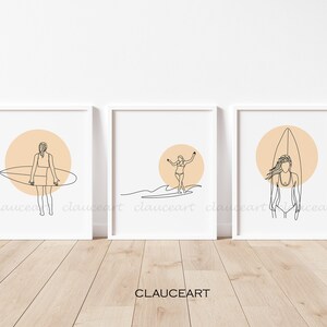 Pu&ograve; includere: Tre stampe minimaliste di arte lineare con una ragazza che fa surf con una tavola da surf davanti a un sole color pesca. Le stampe sono incorniciate in bianco e sono esposte su una parete bianca.