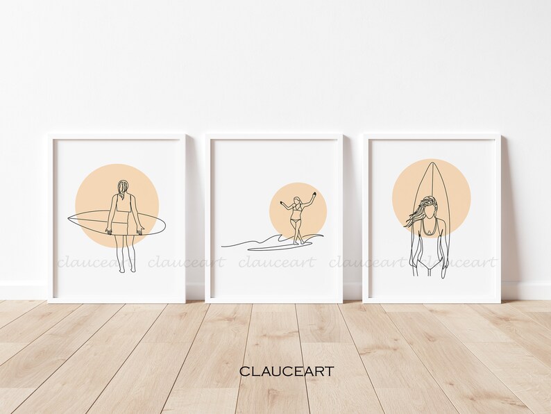 Pu&ograve; includere: Tre stampe minimaliste di arte lineare con una ragazza che fa surf con una tavola da surf davanti a un sole color pesca. Le stampe sono incorniciate in bianco e sono esposte su una parete bianca.
